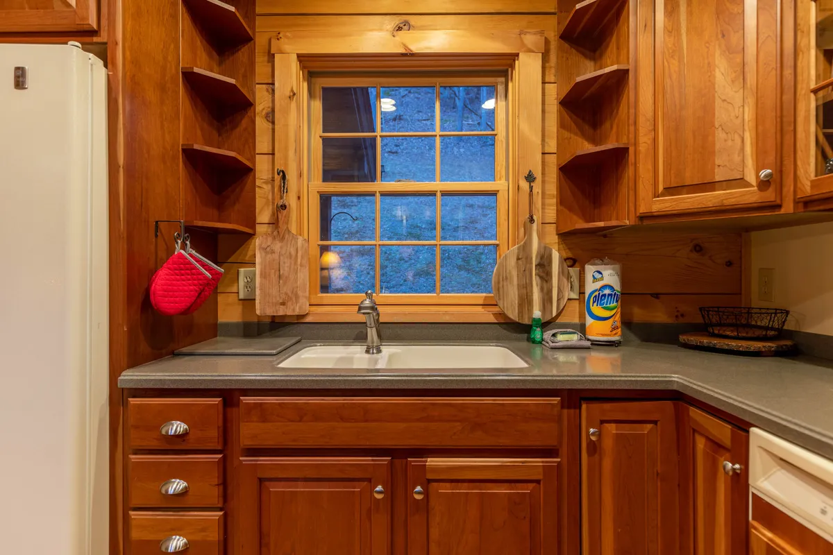 This image captures the kitchen sink under a window framed by wooden cabinets, with utensils and supplies readily at hand. Natural light streams in, creating a welcoming setting for meal prep and cleanup.