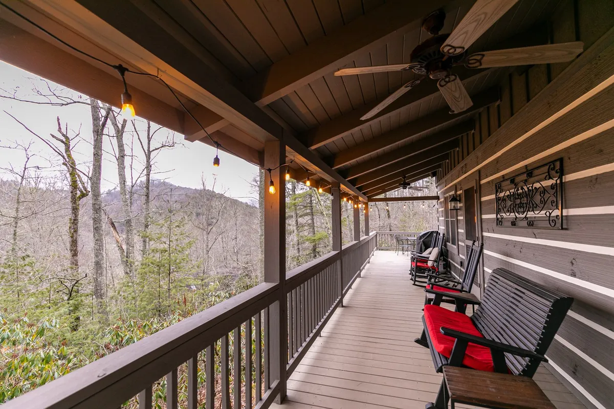 A peaceful exterior deck featuring classic wooden rocking chairs, hanging lights, a wooden railing, and a scenic mountain view in the background. The space feels private and intimate, perfect for sipping coffee or relaxing in the fresh mountain air.
