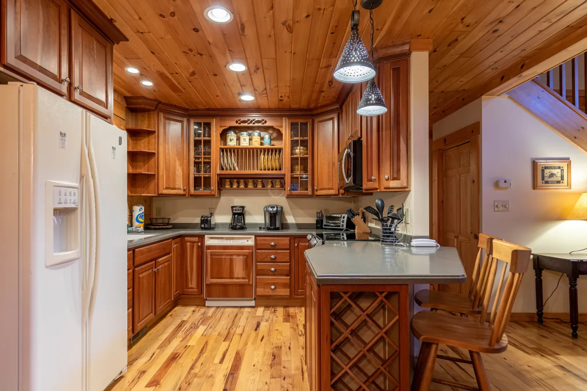 This image focuses on a well-equipped kitchen with wooden cabinetry, a versatile island bar, stainless steel appliances, and open shelving. The layout is practical and inviting, designed for meal preparation, family cooking, and entertaining guests.