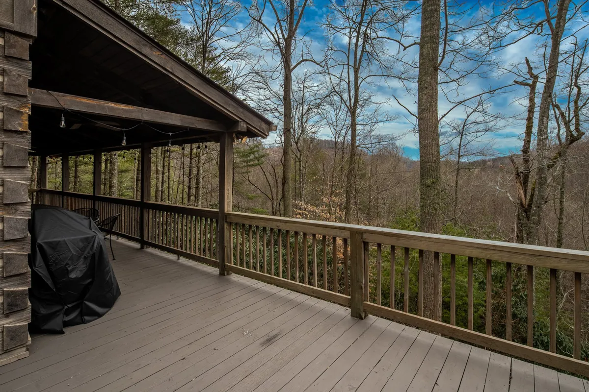 This image features a wooden deck that overlooks surrounding trees and a clear mountain view. The deck itself offers space for relaxation or outdoor dining, inviting guests to immerse themselves in the natural beauty of the Blue Ridge area.