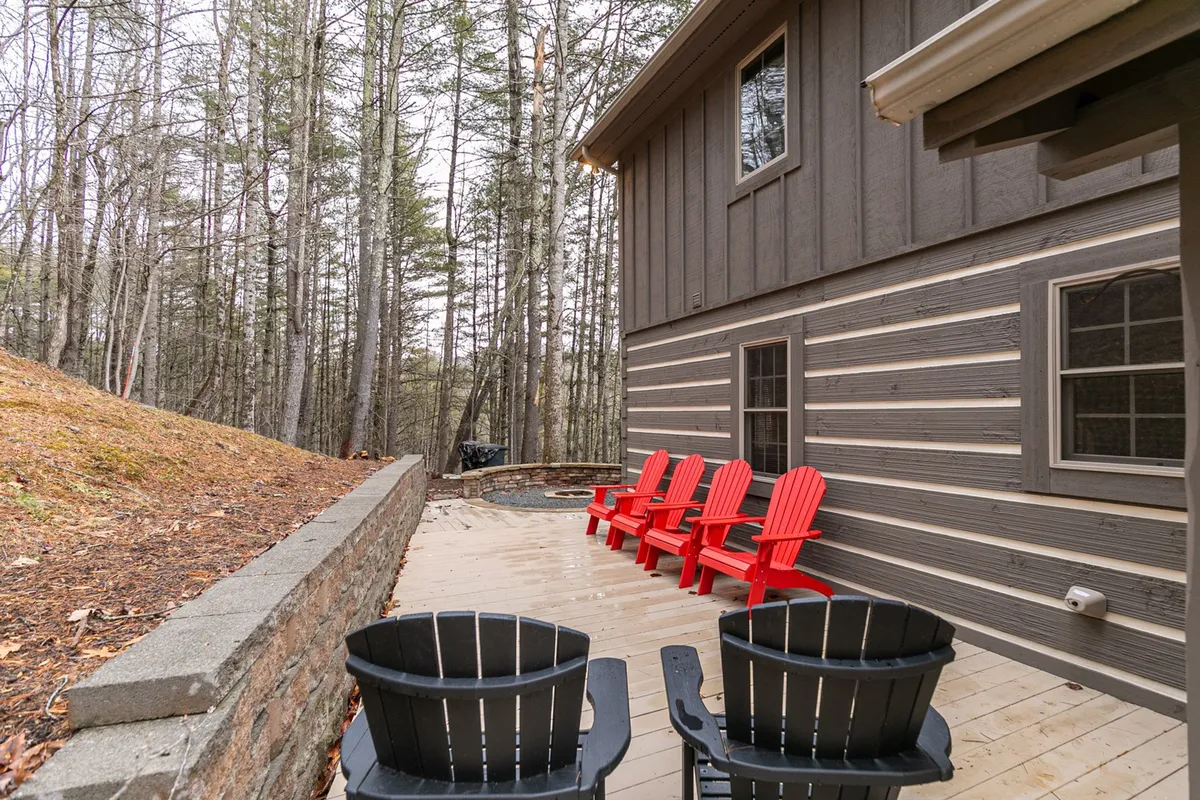 A wooden deck set among trees hosts red and black chairs, offering a relaxed atmosphere for friends to gather, chat, or enjoy a barbecue. The natural setting and ample seating make this deck ideal for socializing amid the scenery.