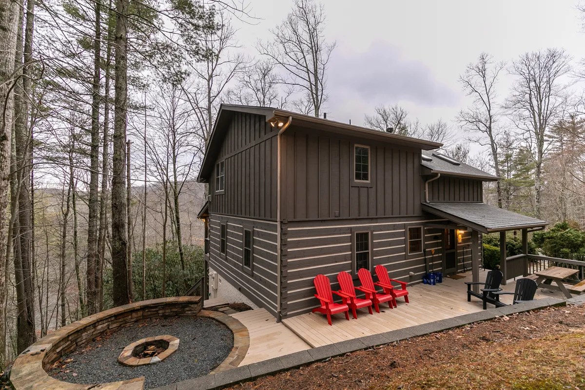 This image features a cozy fire pit area surrounded by red Adirondack chairs set in a wooded environment. The setup encourages gathering, storytelling, and nighttime stargazing, all just steps from nature.